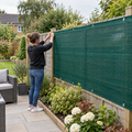 110gsm green HDPE wind barrier mesh being installed on a wooden garden fence in a residential backyard