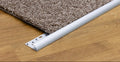 A close-up of a carpet transition strip in white, shown at the corner where a brown textured carpet meets a light wood floor. The logo 'MW Profiles' is visible in the top left corner.