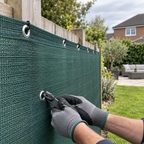 Close-up of green 110gsm HDPE wind barrier mesh with reinforced eyelets being fixed to a garden fence