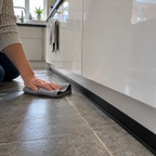 Black PVC kitchen plinth seal installed along the base of modern white kitchen cabinets beside tiled flooring