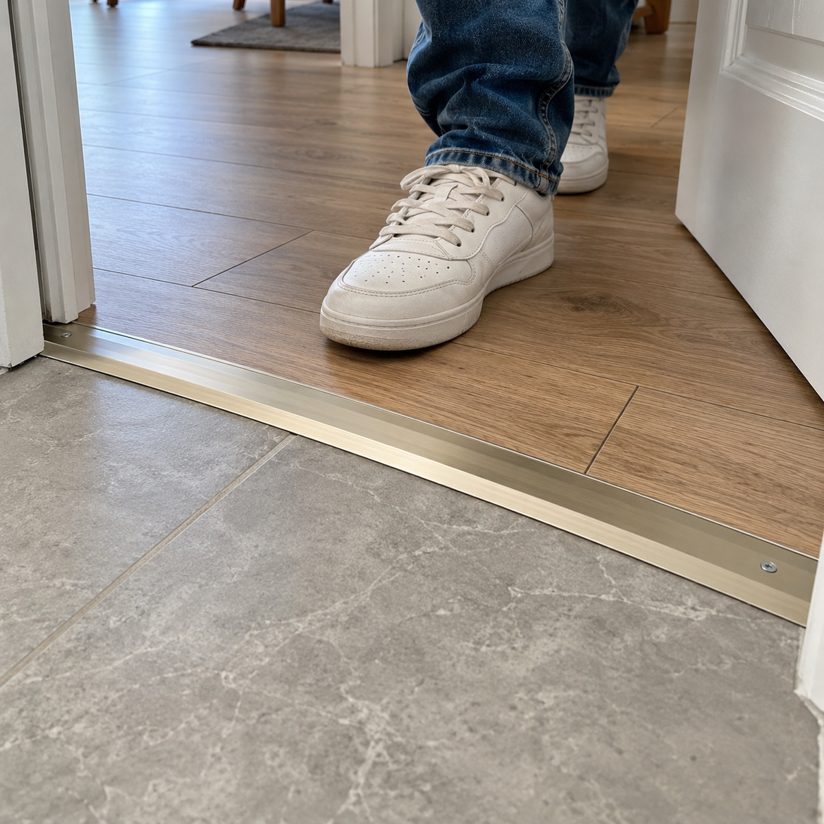 30mm aluminium 4-in-1 floor threshold installed between wood-effect flooring and tiled flooring with a person walking through the doorway