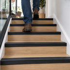 A38 46 x 30mm anodised aluminium non slip rubber stair nosing installed on a modern wood-effect staircase with a person walking upstairs