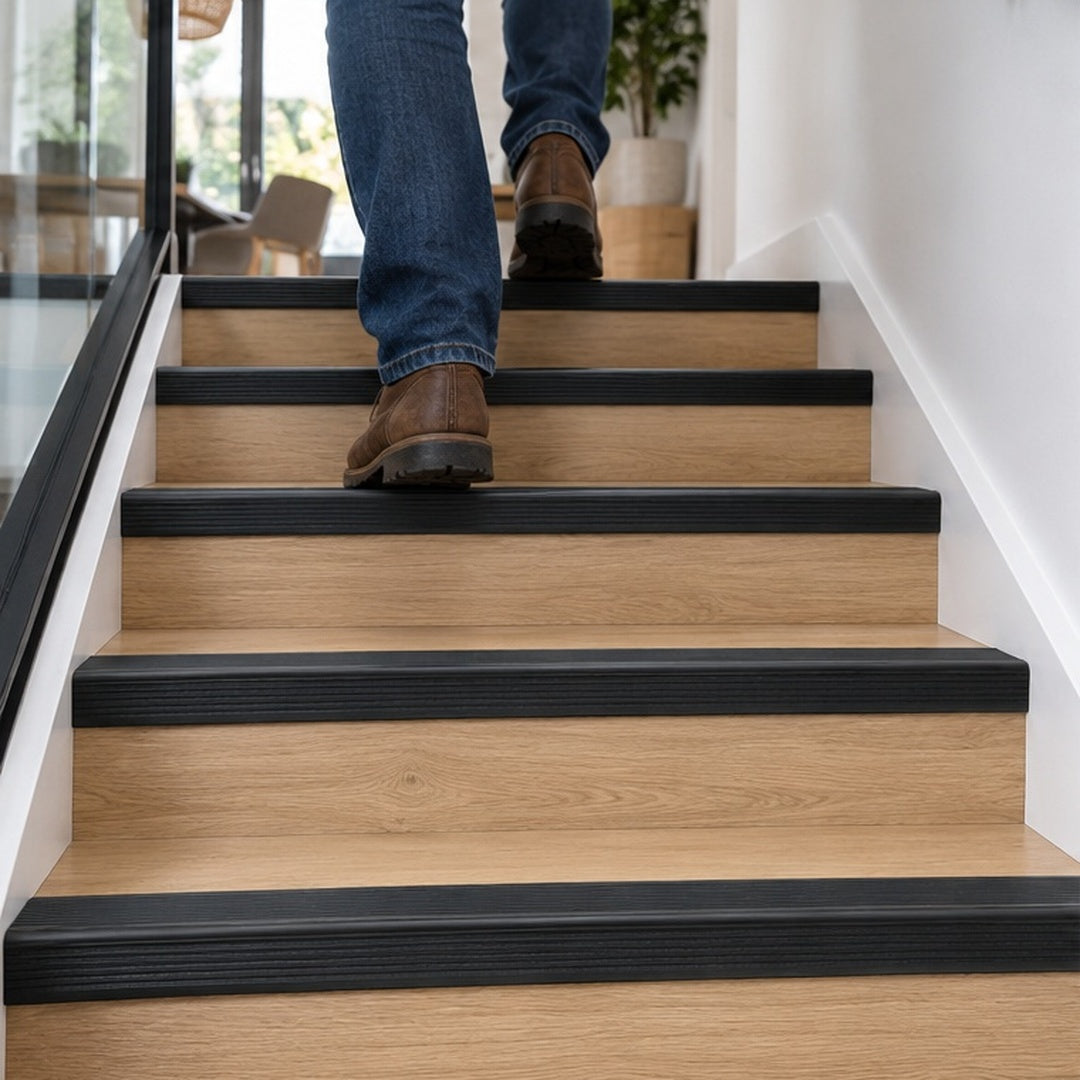 A38 46 x 30mm anodised aluminium non slip rubber stair nosing installed on a modern wood-effect staircase with a person walking upstairs